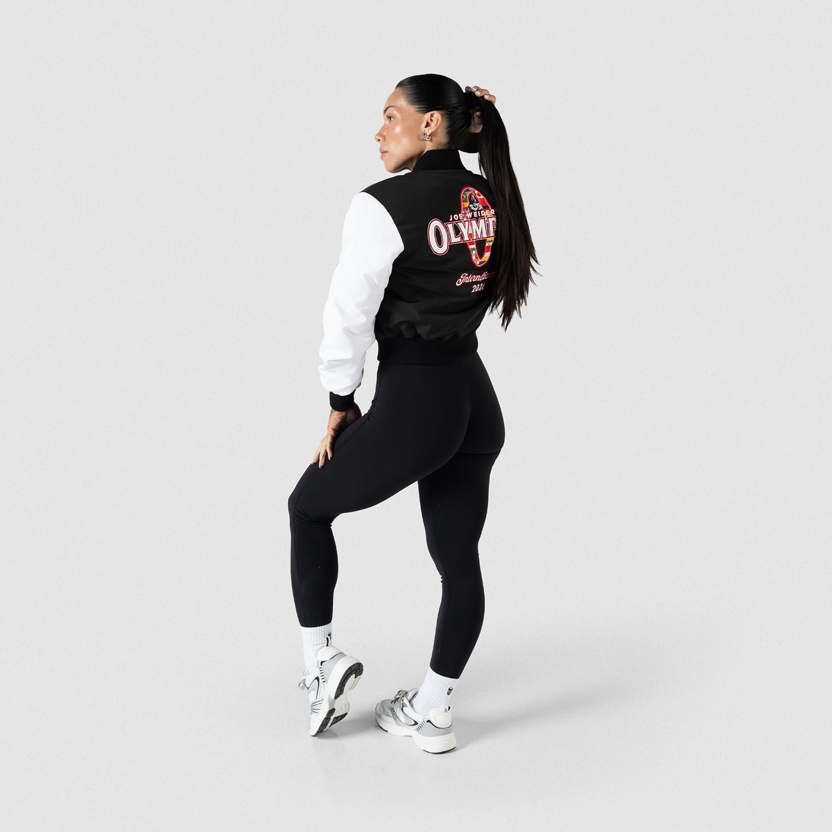International Division Crop Bomber Jacket | Back, angled, model view showcasing the large International Division Olympia Logo on the back of the jacket