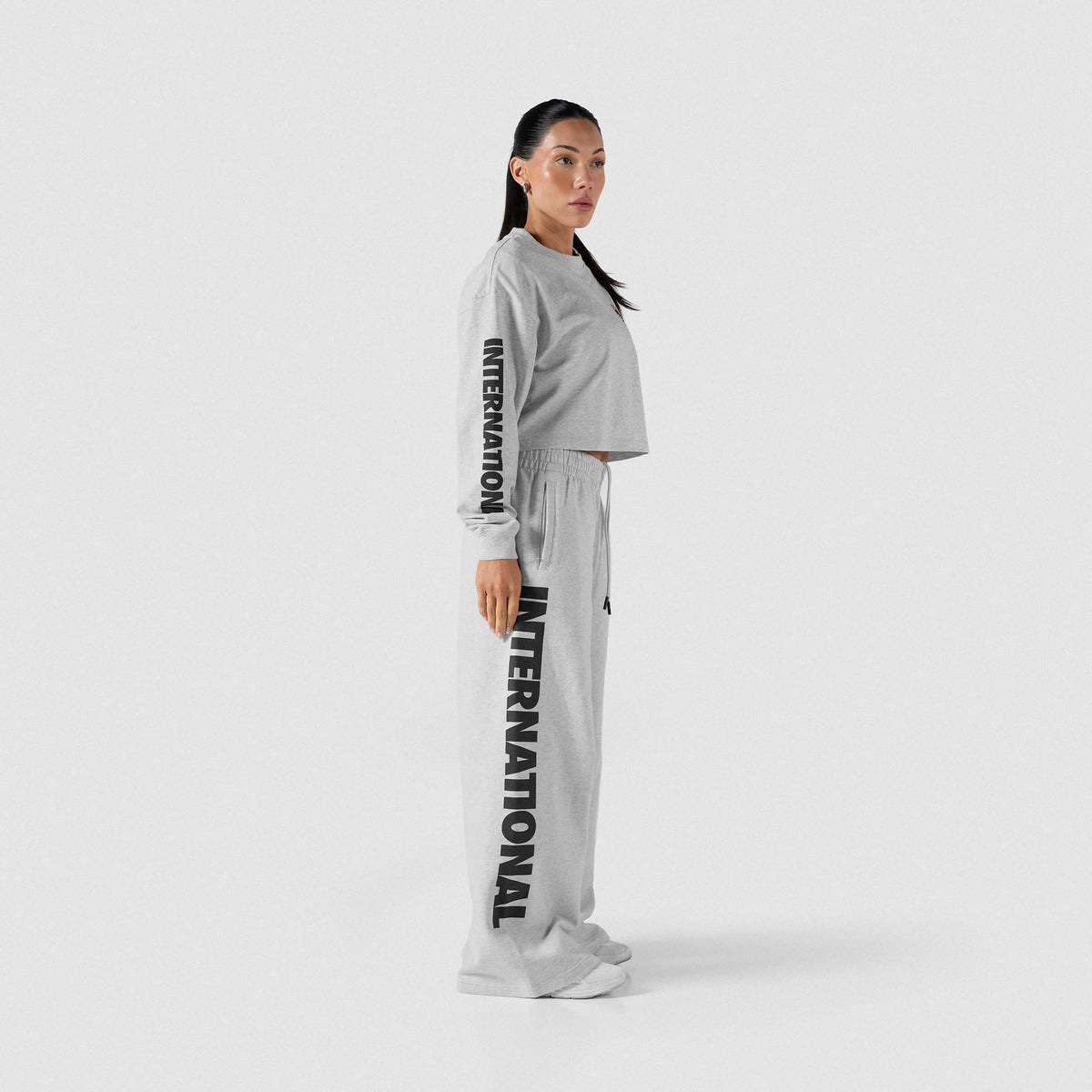 Side view of the Olympia International Division Crop Long Sleeve and matching sweatpants with the "International" wordmark graphic down the side of each product