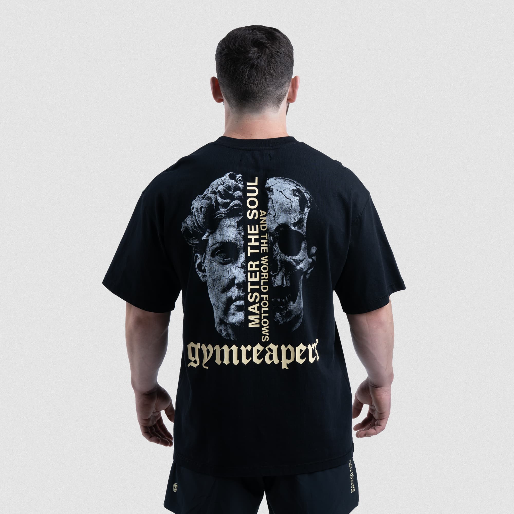 Back view of the Master The Soul Oversized Tee in black, featuring a split skull and statue graphic with vertical campaign text.