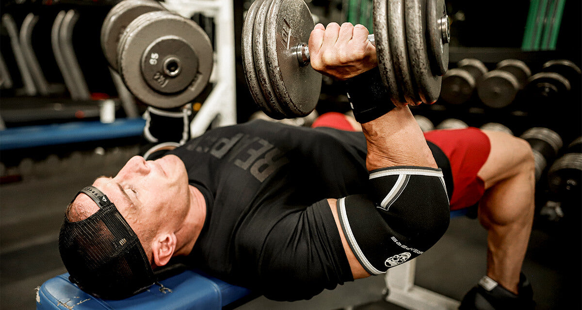 a man lying on a flat bench demonstrating how to perform a dumbbell chest press