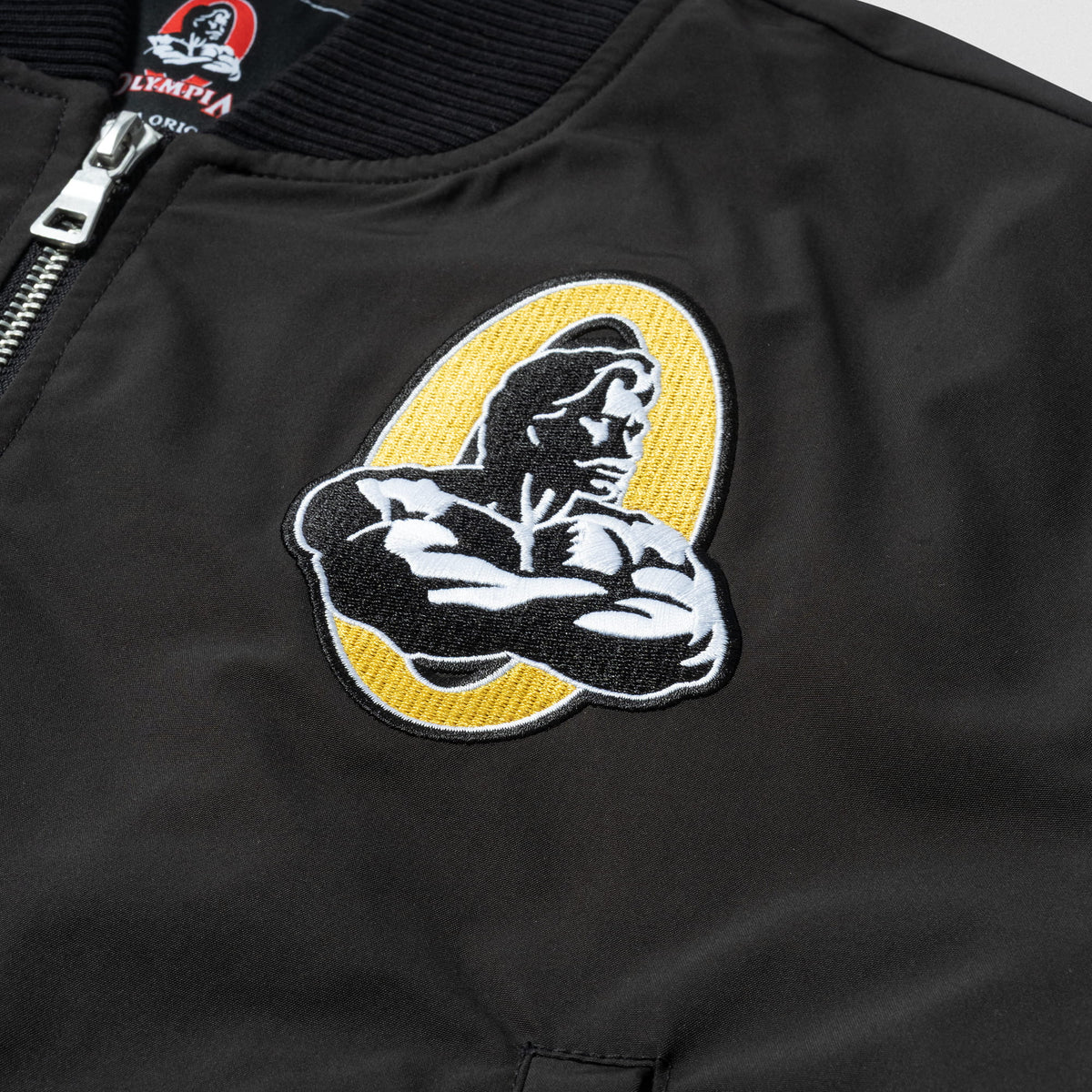 Champions Gold Crop Bomber Jacket | Front left graphic of the Champions Gold Olympia logo