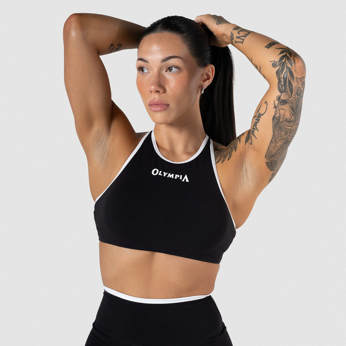 Female model wearing the Olympia High Neck Bra with Black/White contrasting details and "Olympia" wordmark on the chest
