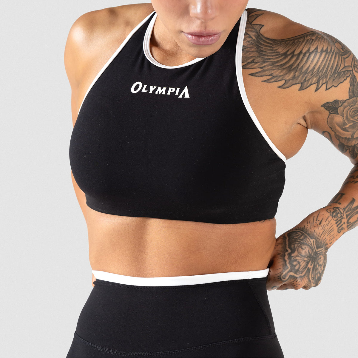 Female model wearing the Olympia High Neck Bra with Black/White contrasting details while adjusting her leggings
