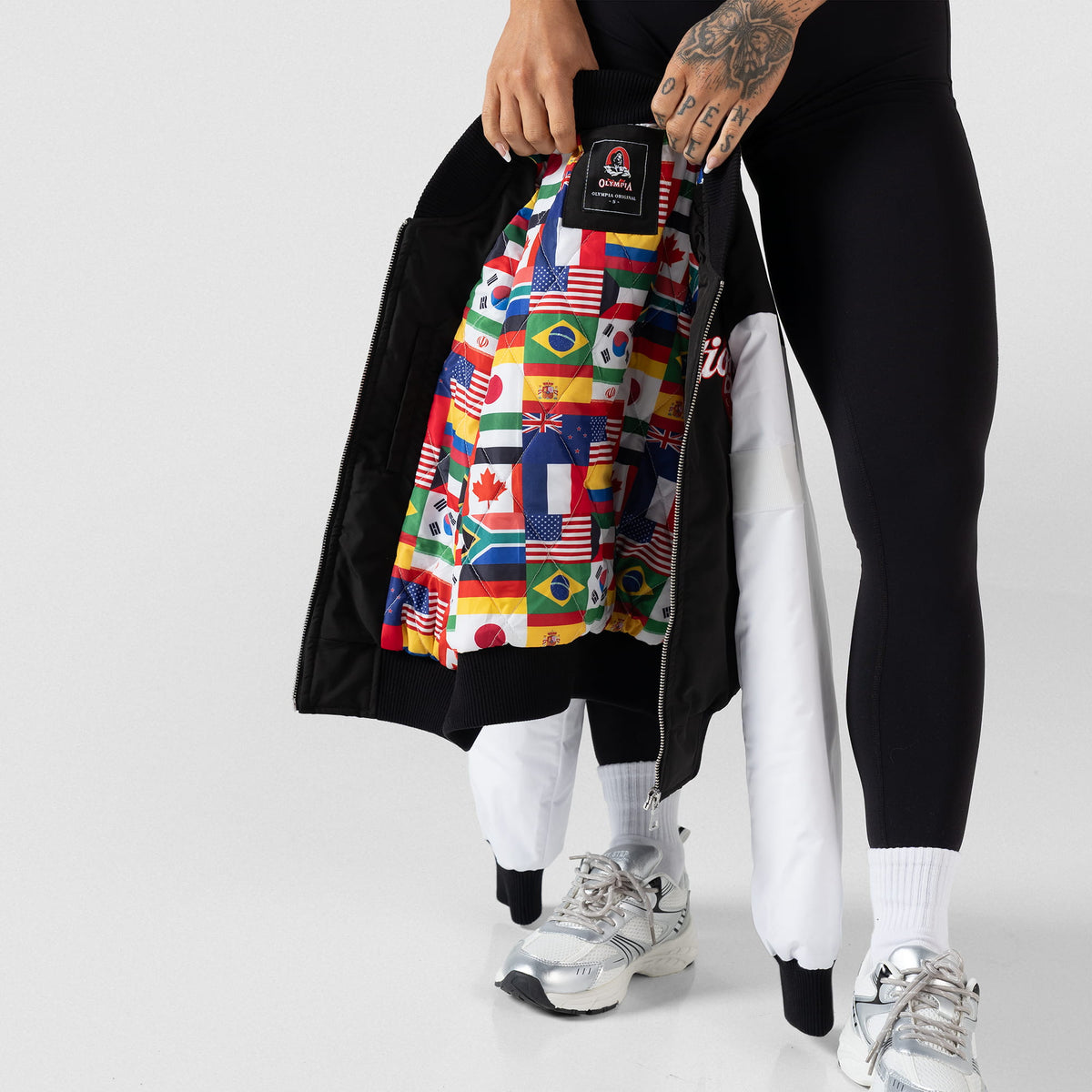 International Division Crop Bomber Jacket | Model holding the jacket at her legs where you can see the opened view and internal flag lining of the International Division
