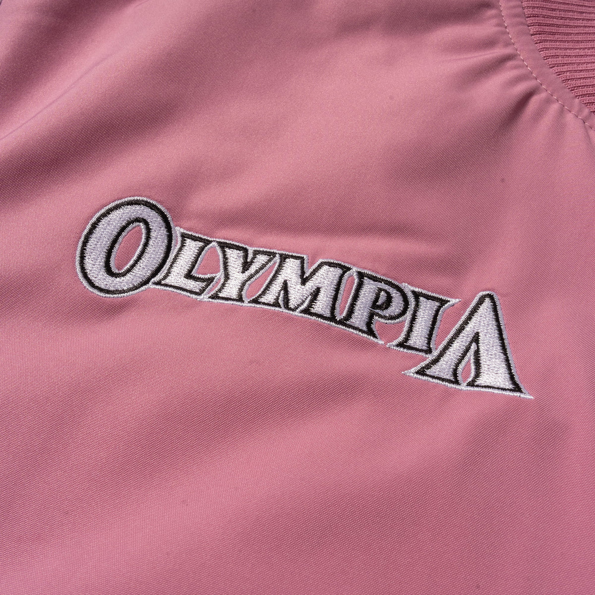 Rose Division Crop Bomber Jacket | Front right chest logo of the wordmark "Olympia" logo in white text on the pink jacket