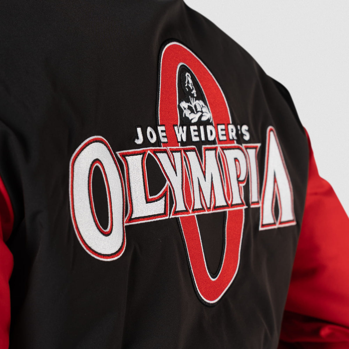 Signature Crop Bomber Jacket | Side view of the back logo that says "Joe Weider's Olympia" in white stitching