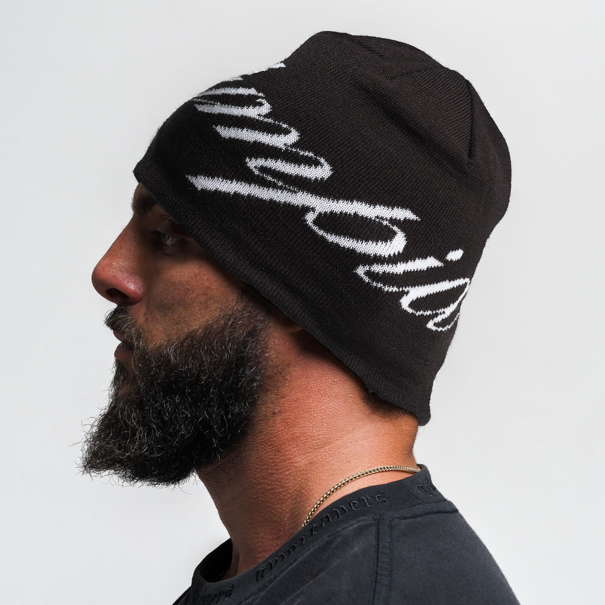 Side view of model wearing the Olympia Script Skull Cap black beanie with white Olympia text 