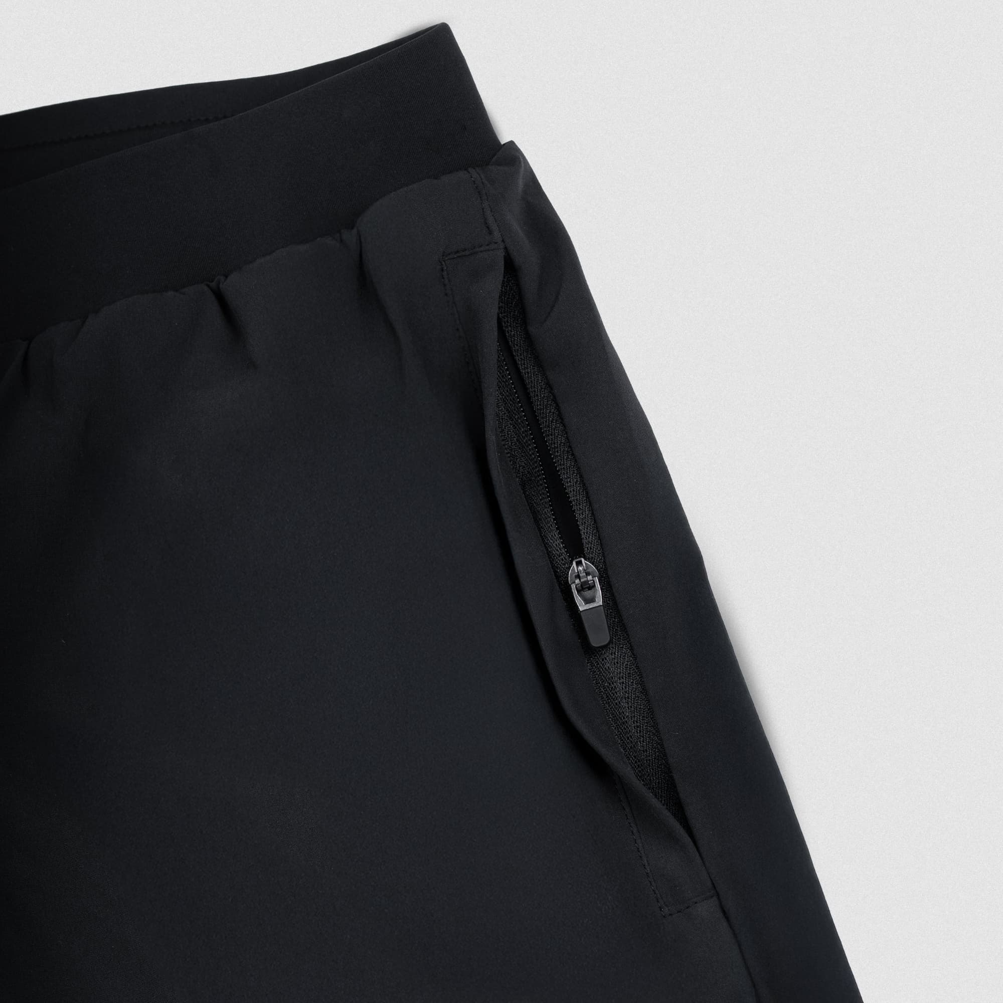 Close-up of zippered pocket on black Master The Soul running shorts showing secure storage and premium performance fabric.