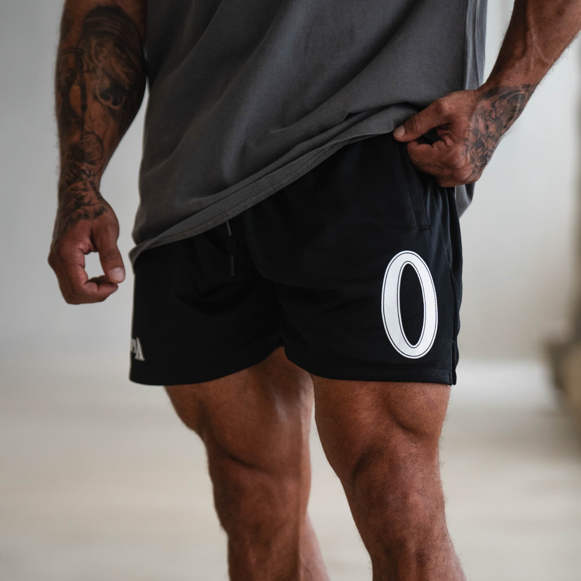 Close-up of black Olympia O Mesh Shorts with large “O” logo on the leg, modeled.