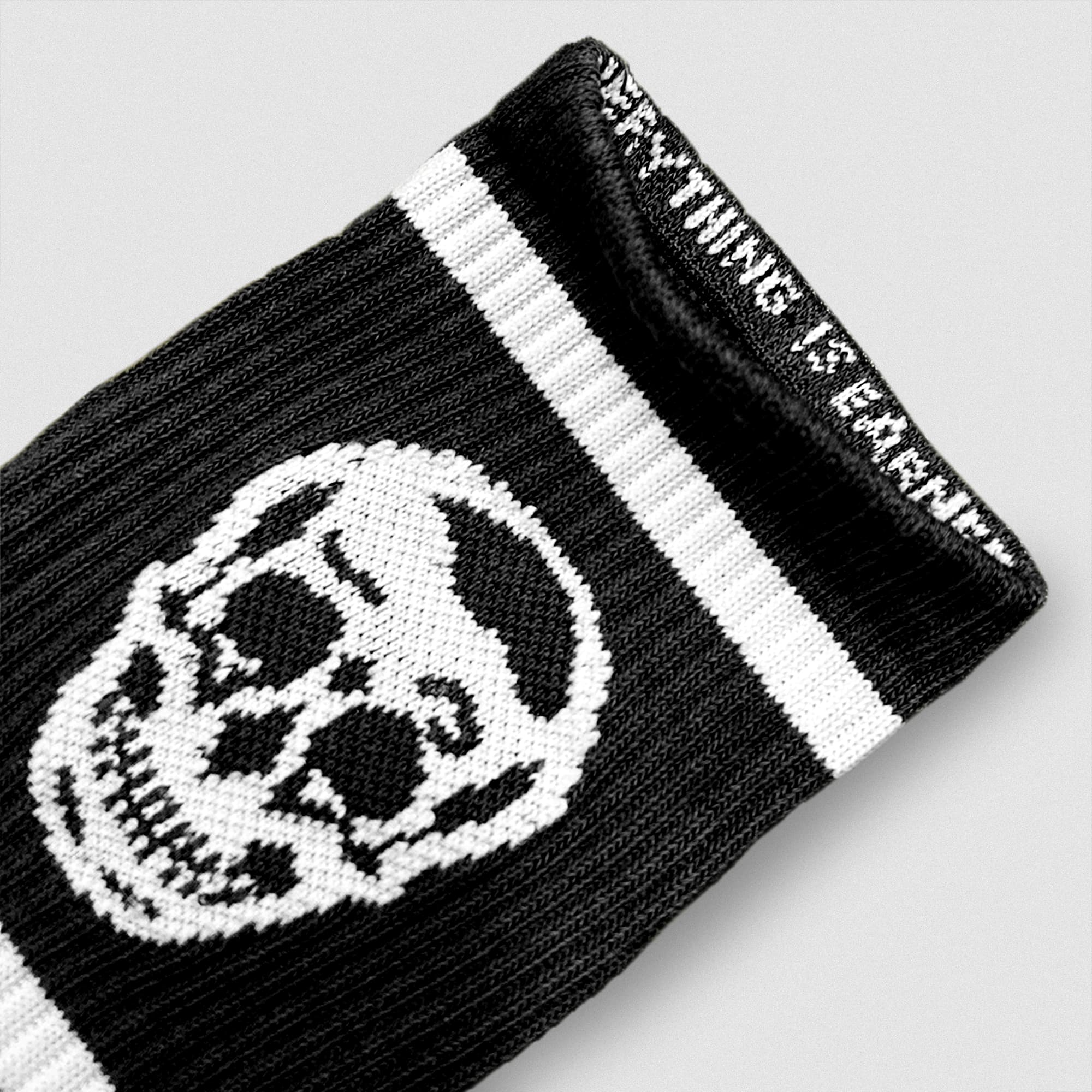 Close-up of a black Gymreapers wristband featuring a white skull design and woven mantra along the inner cuff.