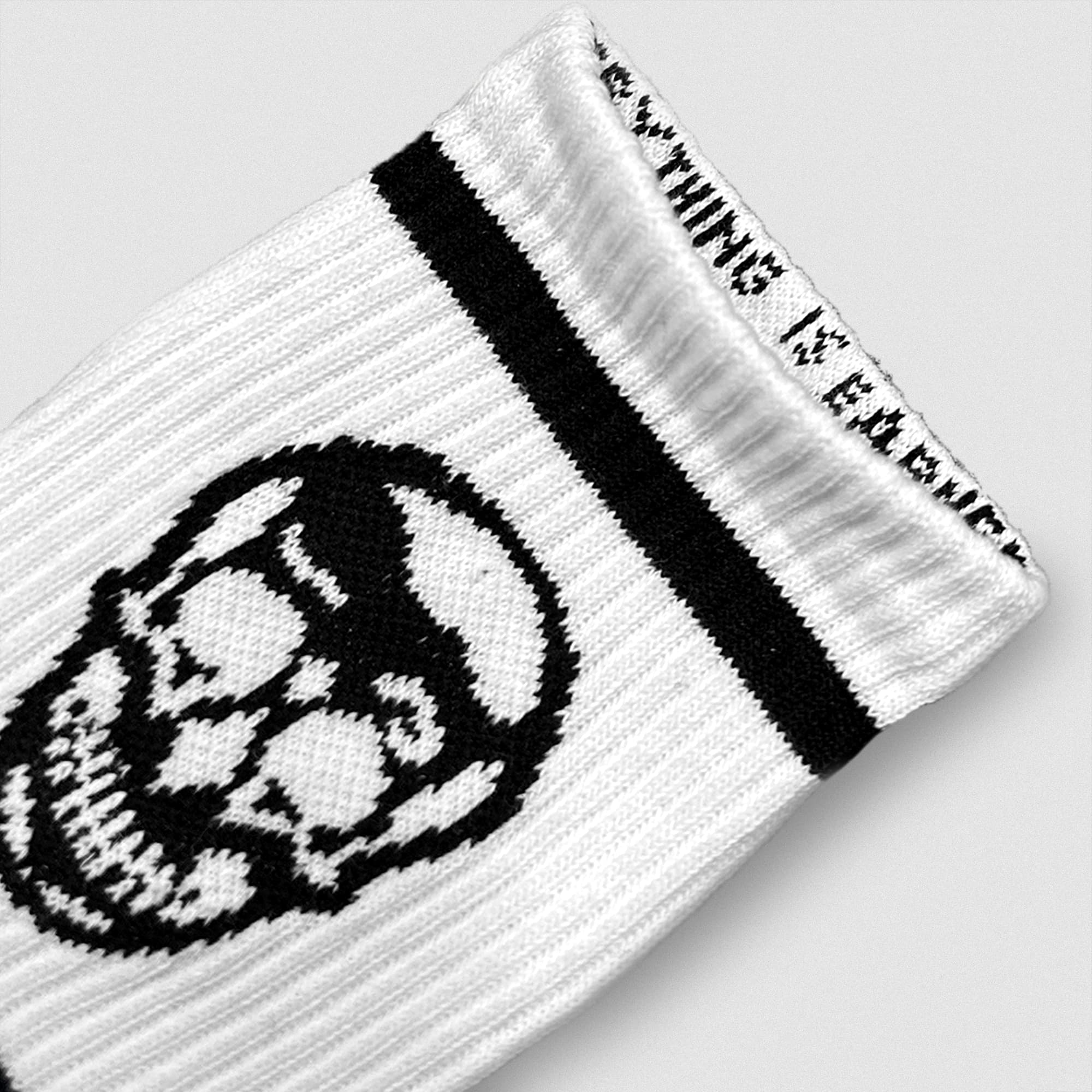 Close-up of a white Gymreapers wristband featuring a black skull design and woven mantra along the inner cuff.